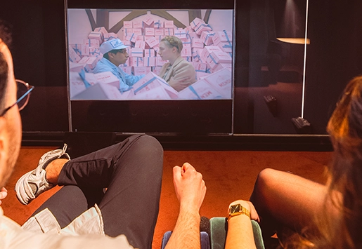 A couple sitting comfortably in front of a large screen showing a scene from The Grand Budapest Hotel.