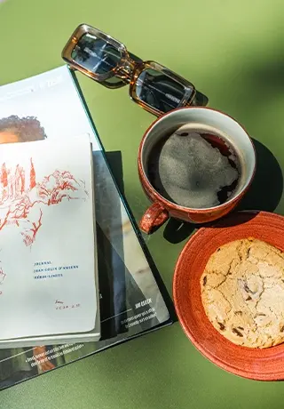 Pause café en terrasse avec tasse de café noir, cookie aux pépites de chocolat, lunettes de soleil et magazine.