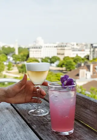 Deux cocktails élégants posés sur le rebord d'un rooftop avec vue panoramique sur la ville.