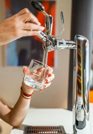 Personne se servant un verre d'eau fraîche à une fontaine à eau en inox.