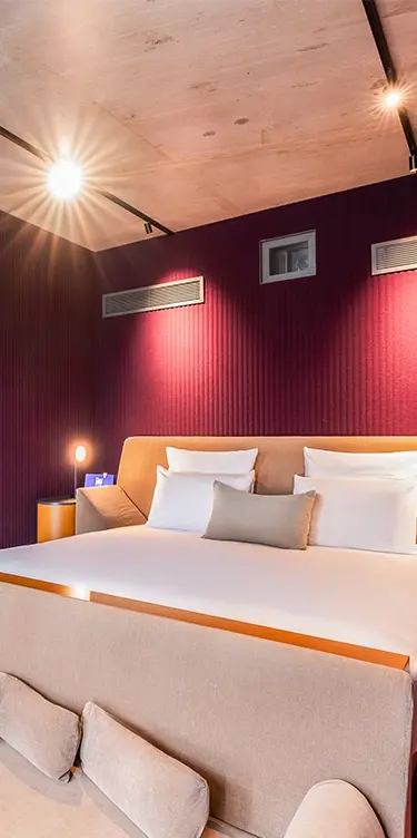 Recadrage vertical resserré sur le lit à tête de lit orange, sous un plafond en bois et un mur cannelé bordeaux éclairé