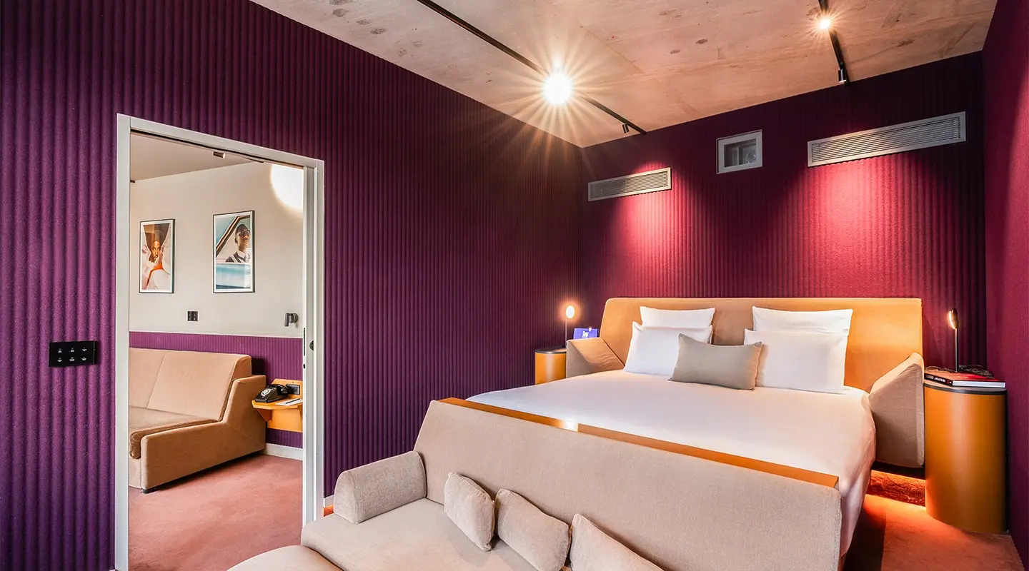 Recadrage vertical resserré sur le lit à tête de lit orange, sous un plafond en bois et un mur cannelé bordeaux éclairé