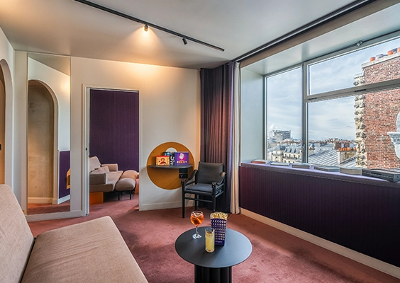 Recadrage plus large de la suite, avec passage arqué vers la chambre violette et large fenêtre offrant une vue sur les toits parisiens
