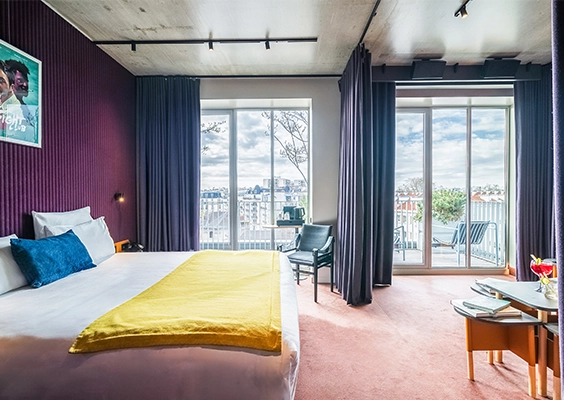 Grande suite d'hôtel avec lit double, coin salon et baies vitrées donnant sur un balcon.