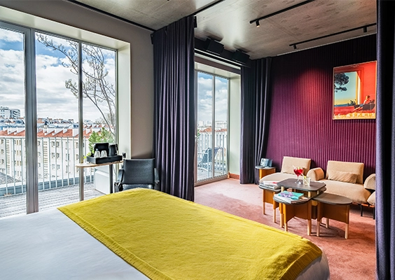 Spacieuse suite d'hôtel avec lit, espace salon moderne et baie vitrée vue sur la ville.