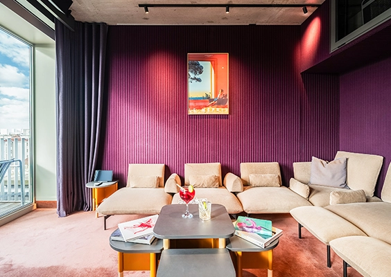 Salon design aux murs violets avec banquettes beiges, tables basses et baie vitrée.