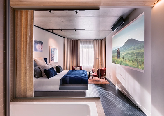 Chambre d'hôtel haut de gamme avec lit double, écran cinéma mural et vue depuis la salle de bains.