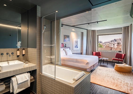 Vue sur une suite d'hôtel design avec baignoire vitrée sur la chambre et coin salon lumineux.