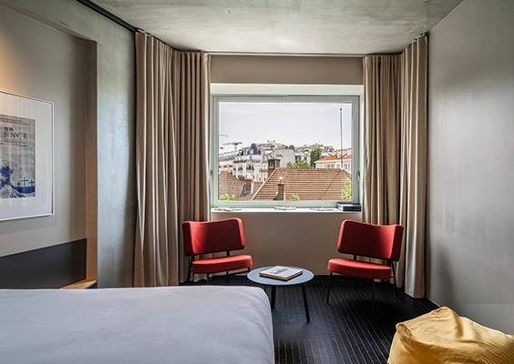Coin salon d'une chambre d'hôtel avec deux fauteuils rouges, une table basse et une fenêtre donnant sur les toits.