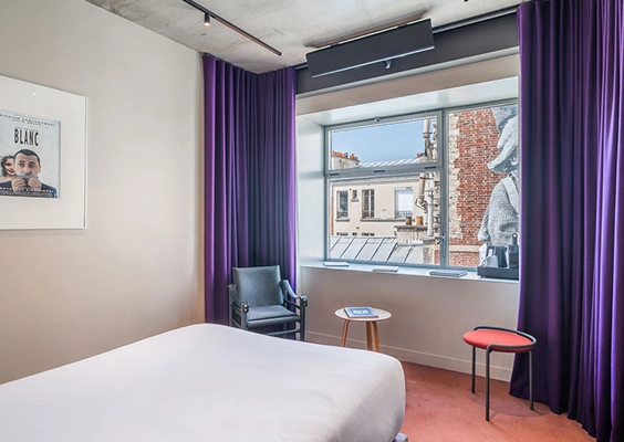 Paire de rideaux violets de chaque côté d'une fenêtre dans une chambre d'hôtel avec un lit et un fauteuil.