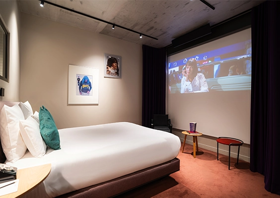 Chambre d'hôtel de luxe avec un lit confortable et un grand écran de projection affichant un film.