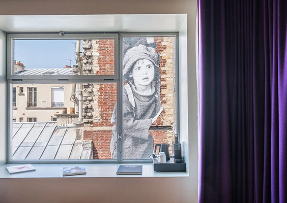 Fenêtre de chambre d'hôtel donnant sur une fresque murale avec un rideau violet à droite.