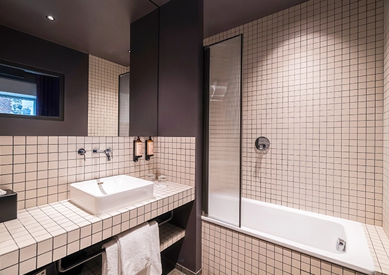 Salle de bains moderne en carrelage quadrillé beige avec baignoire, pare-douche en verre et vasque sur plan.