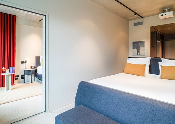 Suite ou chambres communicantes d'hôtel moderne, avec lit double au premier plan et ouverture sur une seconde pièce.