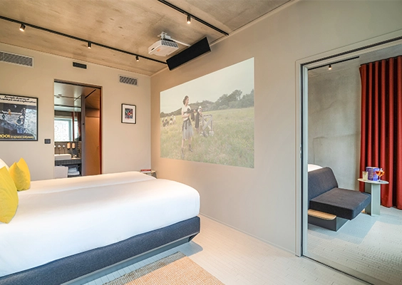 Chambre d'hôtel spacieuse avec vidéo-projecteur mural, vue sur la salle de bains et accès à une pièce adjacente.