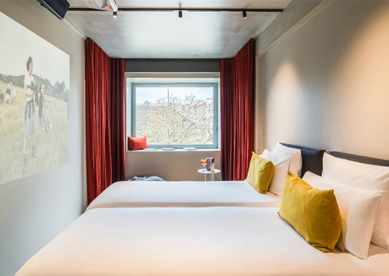Chambre double ou jumeaux au design moderne, dotée d'une projection vidéo sur le mur latéral, de rideaux rouges et de coussins jaunes.