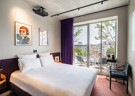 Chambre d'hôtel lumineuse avec lit double, rétroprojecteur et terrasse extérieure aménagée.