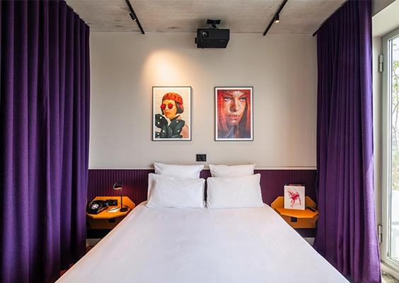 Chambre d'hôtel élégante avec lit double, rideaux violets et rétroprojecteur au plafond.