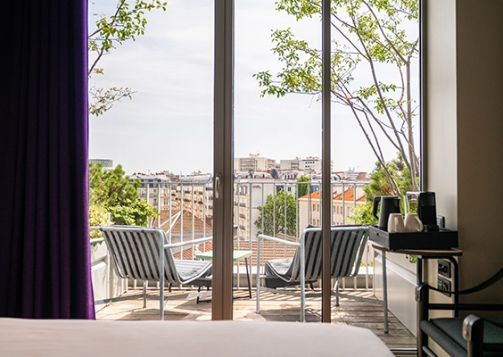 Vue depuis une chambre d'hôtel sur une terrasse privée aménagée de transats, avec vue dégagée sur la ville.