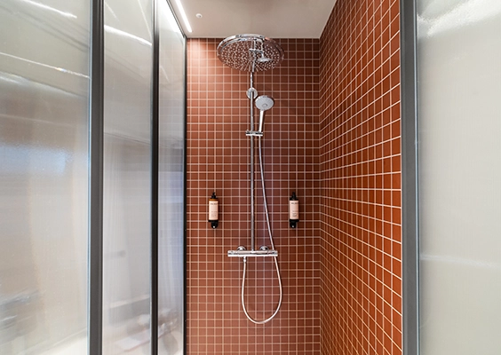 Cabine de douche moderne habillée de petits carreaux terracotta, équipée d'une colonne de douche chromée avec pommeau effet pluie.