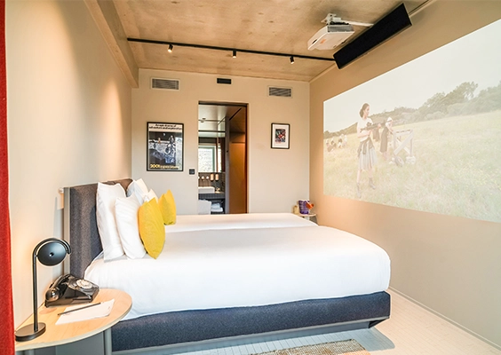 Chambre d'hôtel moderne équipée de deux lits simples, avec rétroprojecteur au plafond et vue traversante vers la salle de bains.