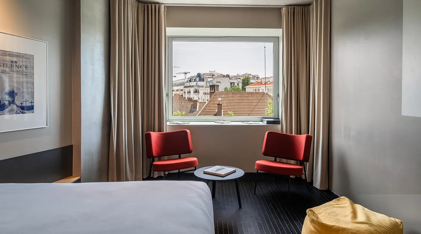 Tight vertical crop focusing on the red armchairs and the panoramic window overlooking the Parisian rooftops