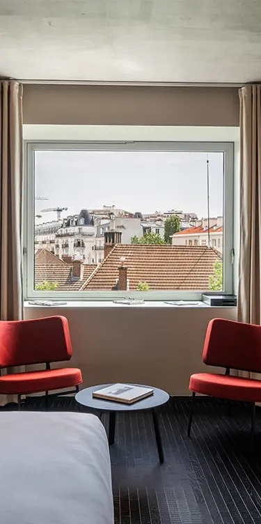 Tight vertical crop focusing on the red armchairs and the panoramic window overlooking the Parisian rooftops