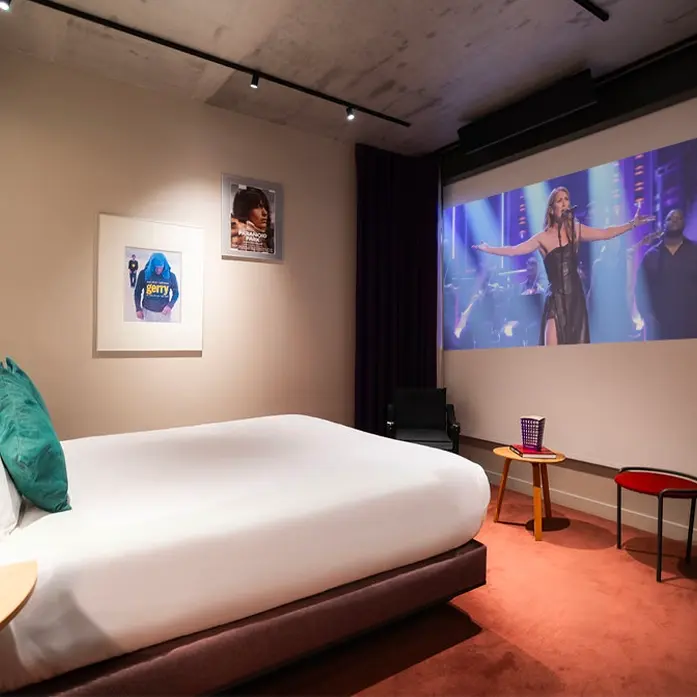 Chambre d'hôtel avec lit double et écran de projection mural.
