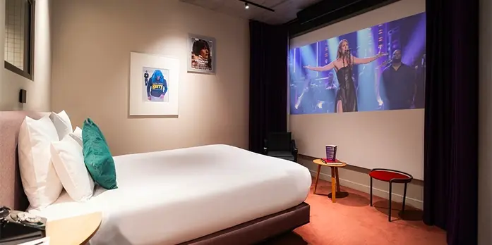 Chambre d'hôtel avec lit double et écran de projection mural.