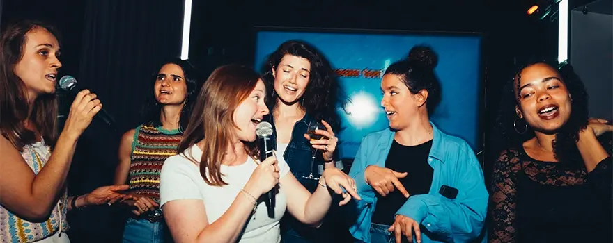 Groupe de jeunes femmes chantant joyeusement au karaoké avec des micros lors d'une soirée entre amies