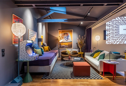 Cozy loft-style living room featuring exposed beams, comfortable sofas, a retro arcade cabinet, and a projector screen.