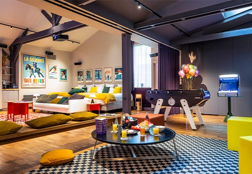 Spacious, cozy hotel loft featuring a sleeping area, foosball table, arcade cabinet, and a lounge corner perfect for drinks.