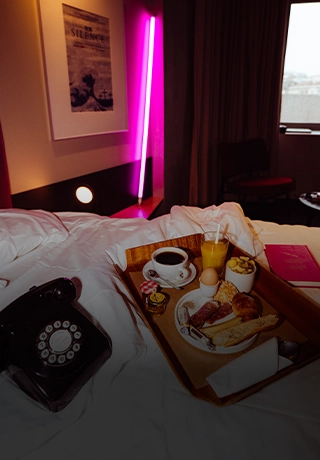 Plateau petit-déjeuner garni servi sur un lit d'hôtel avec téléphone vintage et néon rose.