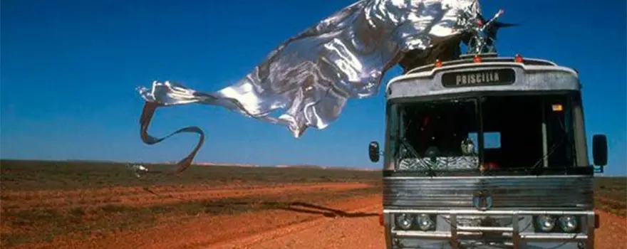 Bus qui roule dans un désert de sable rouge avec un drap métallique qui vole