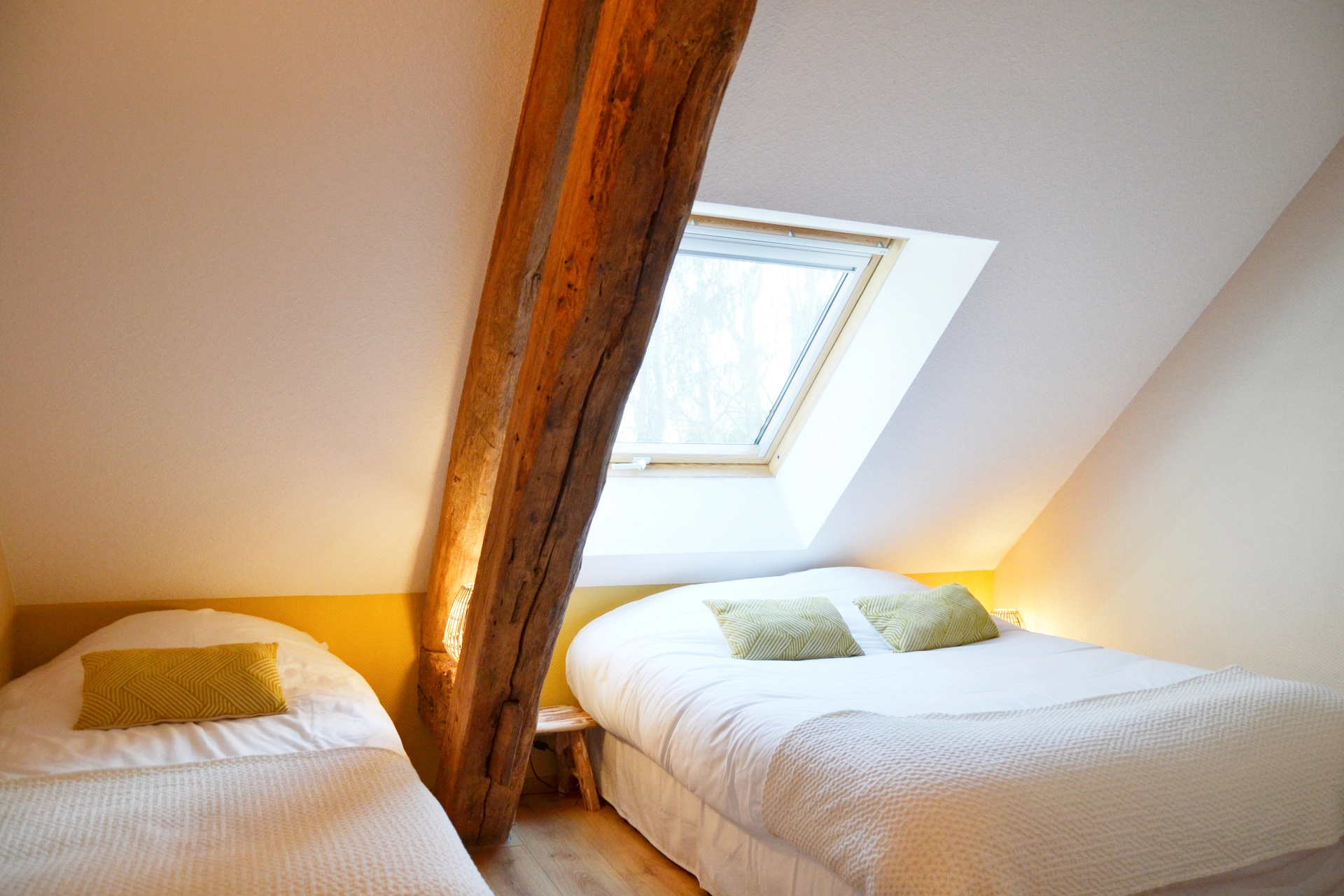 Triple attic room with a double bed and a single bed separated by a solid wooden beam and a skylight.