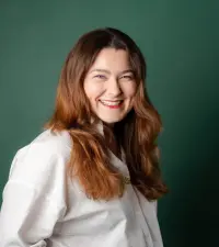 Portrait professionnel d'une femme souriante aux cheveux auburn, vêtue d'une blouse blanche, sur fond vert
