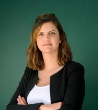 Portrait professionnel d'une femme aux cheveux châtains, veste noire et bras croisés, sur fond vert
