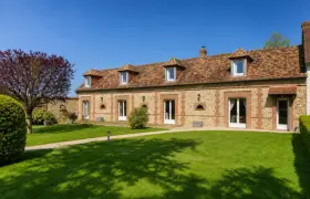 Façade d'un corps de ferme normand en pierre et brique avec lucarnes, pelouse verdoyante et arbre à feuilles pourpres