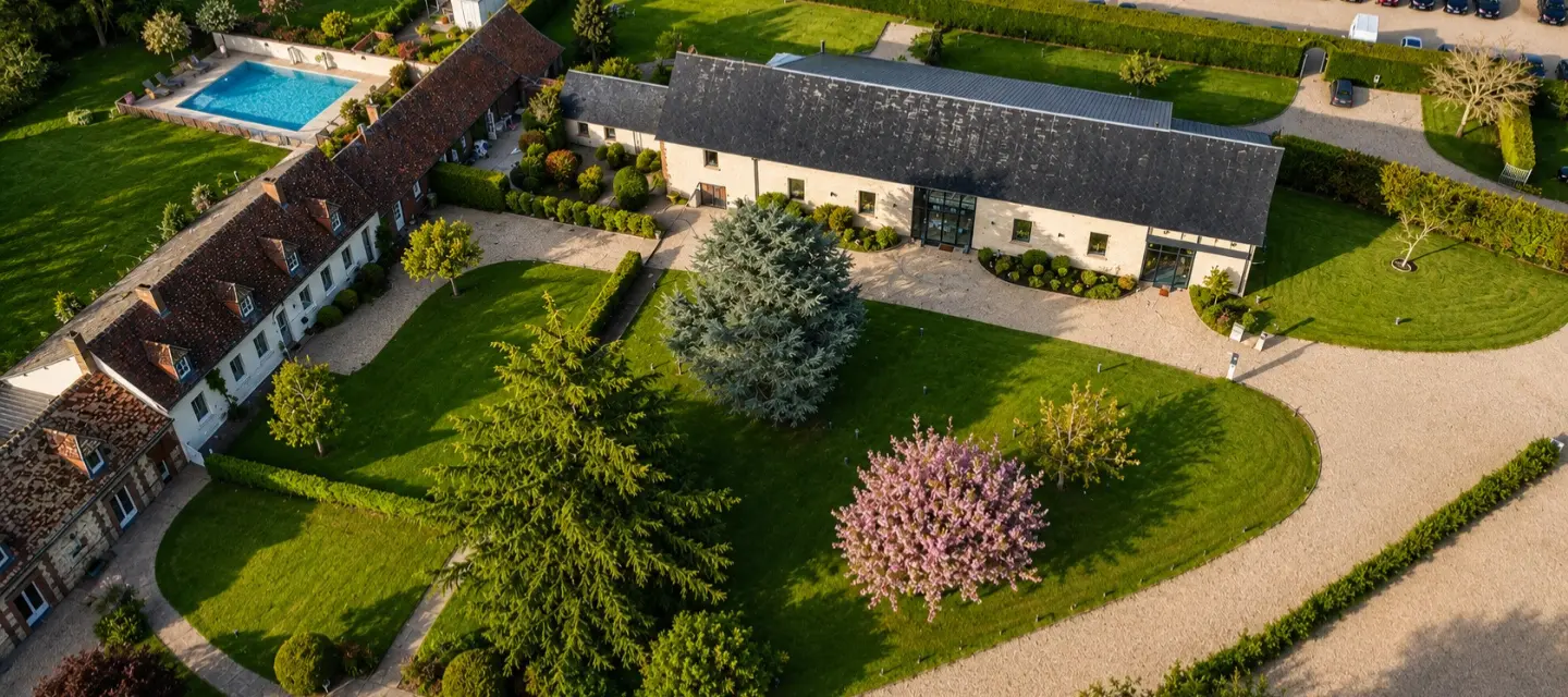 Vue aérienne du domaine au coucher du soleil, avec pelouse arborée, piscine extérieure, grange rénovée et allées en gravier