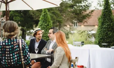 Groupe de personnes élégantes conversant autour d'une table sous un parasol blanc lors d'un événement en plein air