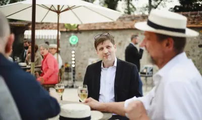 Invités discutant autour d'une table avec des verres de vin blanc lors d'un cocktail en plein air devant un bâtiment en pierre