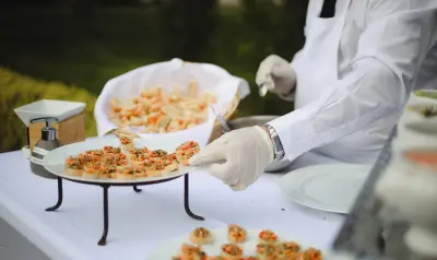 Serveur en tenue blanche dressant un plateau de canapés aux légumes lors d'un service traiteur en plein air