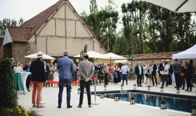 Cérémonie d'inauguration avec ruban rouge au bord d'une piscine, invités rassemblés devant une grange à colombages