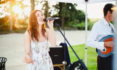 Chanteuse en robe fleurie se produisant en plein air au coucher du soleil, accompagnée d'un guitariste