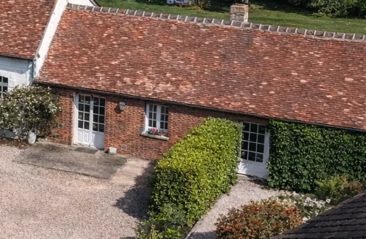 Facade of a renovated stone barn surrounded by well-tended gardens, with flowering rose bushes in the foreground and a blue sky