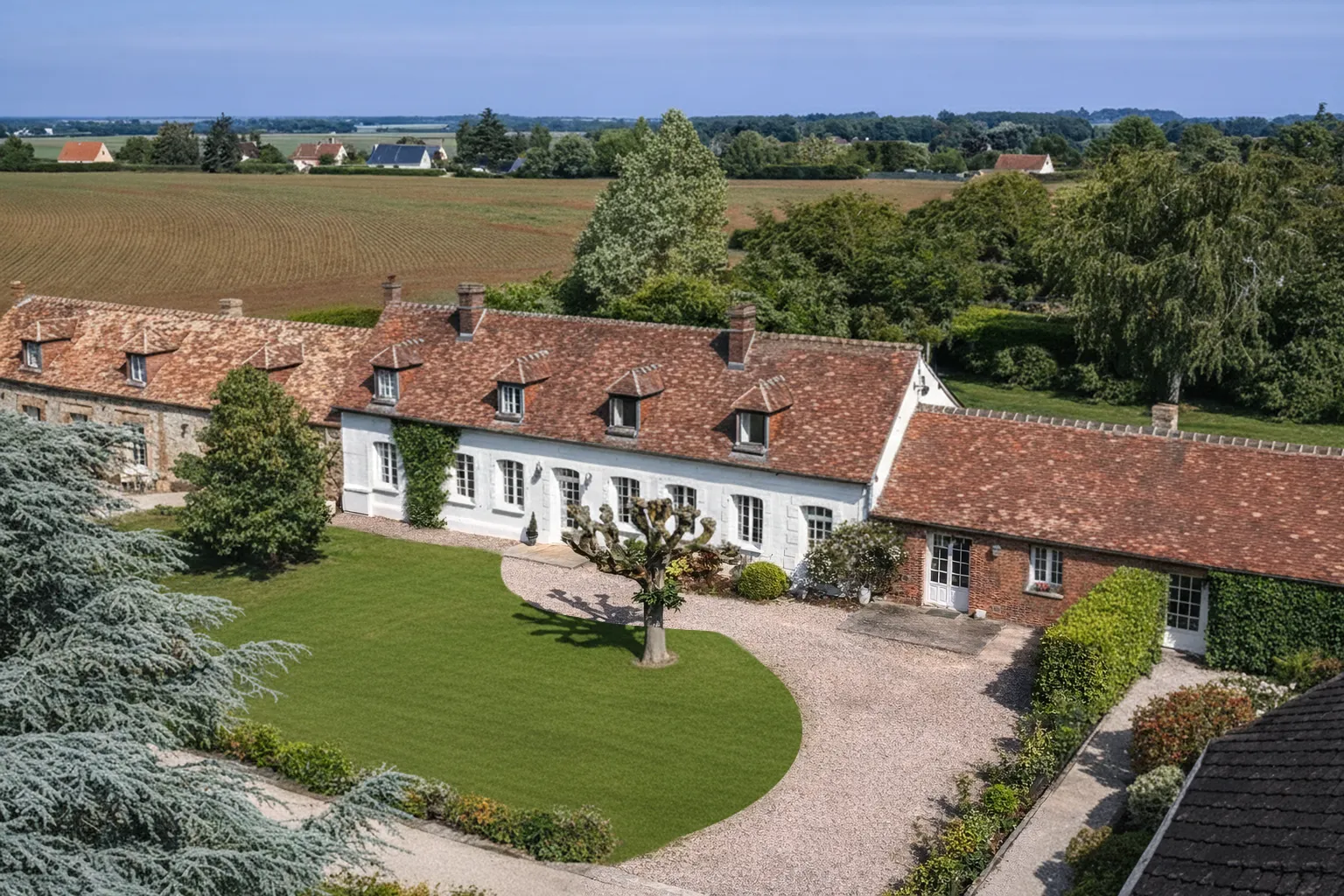 Vue aérienne d'un domaine rural en forme triangulaire, entouré de champs et d'arbres, avec cour intérieure et bâtiments en pierre