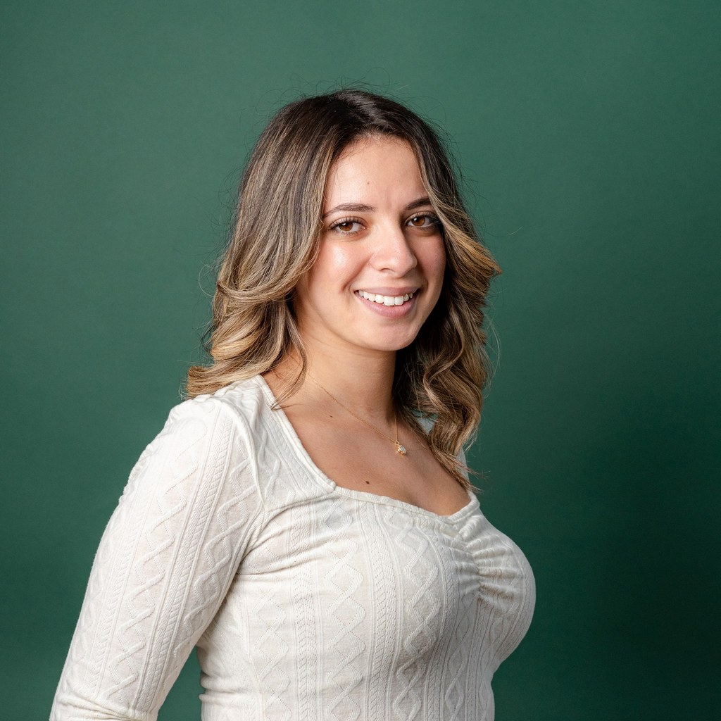 Portrait professionnel d'une femme souriante aux cheveux auburn, vêtue d'une blouse blanche, sur fond vert