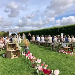 Cérémonie de mariage en plein air avec invités assis sur des bancs en bois et décorations florales.