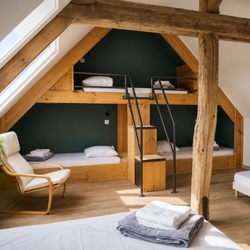 Chambre avec lits superposés intégrés en bois, escalier, fauteuil et linge plié sur lit.
