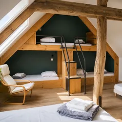 Chambre avec lits superposés intégrés en bois, escalier, fauteuil et linge plié sur lit.